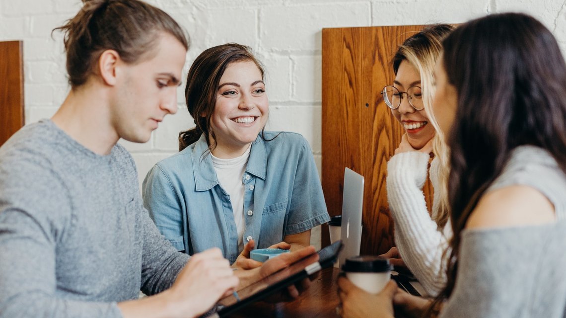 Drei Studentinnen und ein Student sitzen im Café und reden miteinander.