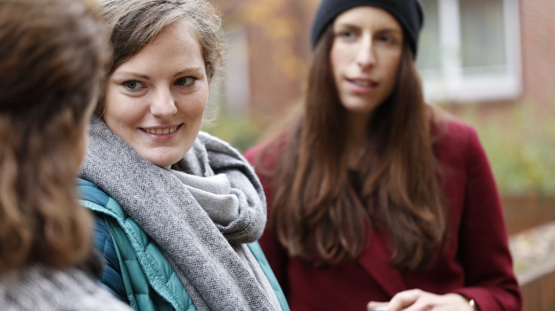 Drei junge Frauen stehen vor der Hochschule und unterhalten sich.