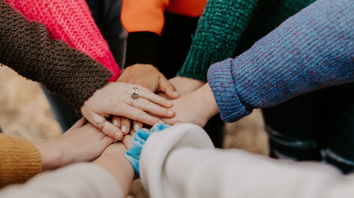 Acht Hände von acht Menschen liegen aufeinander.